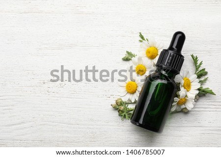 Flat lay composition with bottle of chamomile essential oil and space for text on white wooden background