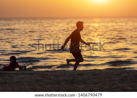 Father and kid playing on the beach at the sunset time. Concept of friendly family