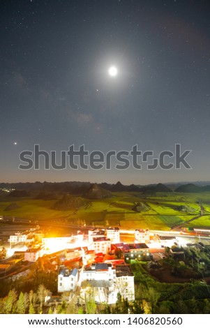 The moon and the miky way over the canola fields and town with many mountians, Louping country, Yunnan, China.