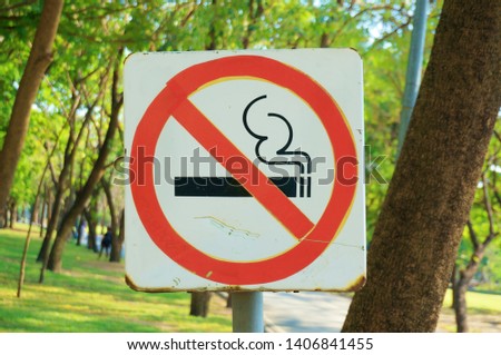 A photo of old metal no smoking sign in the park with natural green background, close up