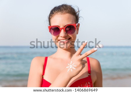 Young woman is showing peace gesture and has sun shape on her hand at the beach.