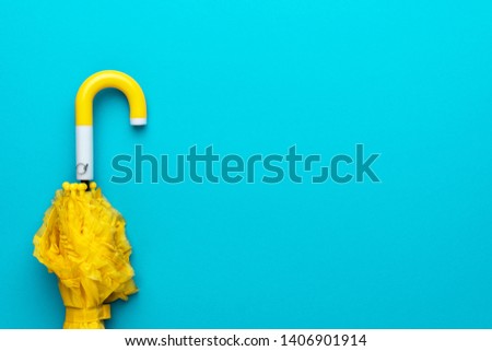 folded yellow umbrella on turquoise blue background. flat lay image of yellow umbrella with copy space. minimalist photo of folded umbrella
