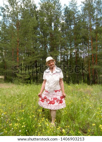 Pretty Ukrainian blonde woman in a hat and summer dress posing in wildflowers on a meadow in the forest