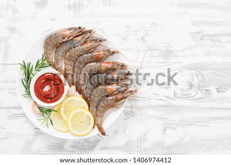 Raw shrimps in white plate with lemon and tomato sauce.
