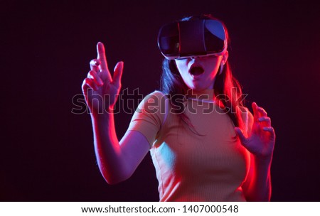 Young woman wearing virtual reality device over dark background. She touch empty virtual screen.