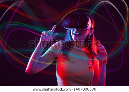 Young woman wearing virtual reality device over dark background. Flare effect, blurred colours around her.