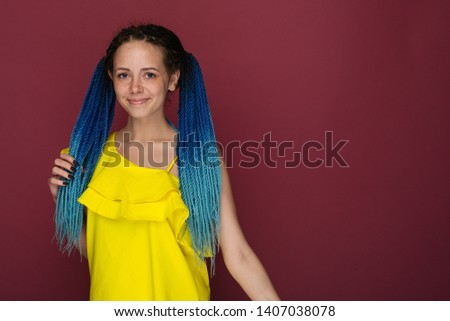 Portrait of a cheerful girl with freckles and blue braided hair against a ruby background