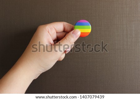 A hand holding a rainbow pin. 