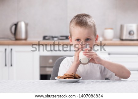 Happy little boy sitting at the table in the kitchen and drinking healthy milk glass and sweet cookies. Tasty and delicious snack.