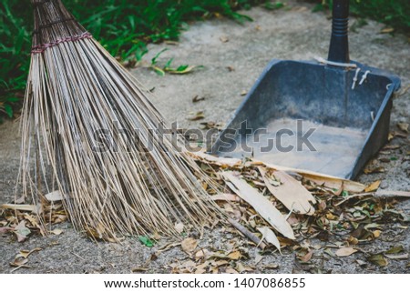 Coconut broom and dustpan are sweeping dry leaves that are blown down on the lawn after rain storms on Saturday evening.