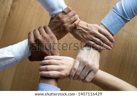 Diverse business people team connected grasping hands holding each other wrists in circle, loyalty help in teamwork concept, professional trust power support unity solidarity, close up top view above Royalty-Free Stock Photo #1407116429
