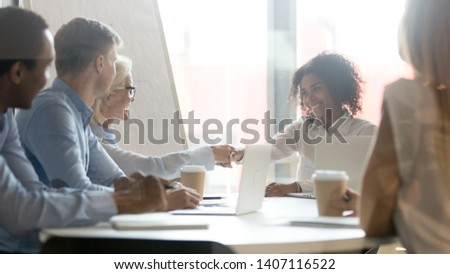 Smiling african female leader handshake partner client making commercial deal agreement at team meeting or group negotiations sitting at conference table shake hands thank for collaboration, respect Royalty-Free Stock Photo #1407116522