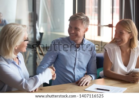Old female broker bank manager handshake happy young couple clients make business insurance investment deal, family customers sign mortgage loan contract shake hand of realtor insurer meeting advisor