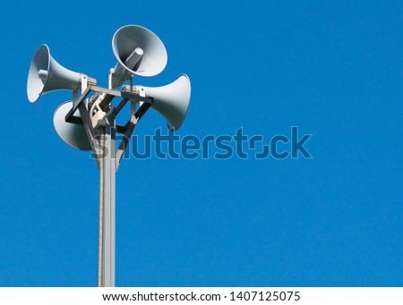 A tall column with four gray loudspeakers in a circle against a clean blue sky. Hazard warning system. The possibility of placing your test or image. Royalty-Free Stock Photo #1407125075