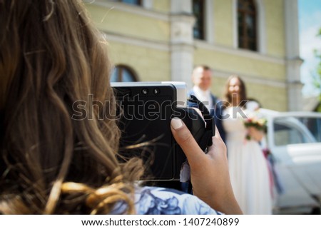 Girl holding instant still camera takes pictures of the bride and groom at wedding