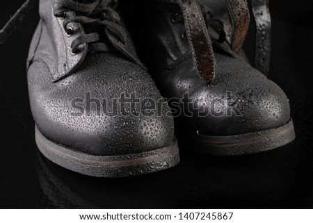 Black military boots and rain drops. Well-preserved old boots for soldiers. Dark background.