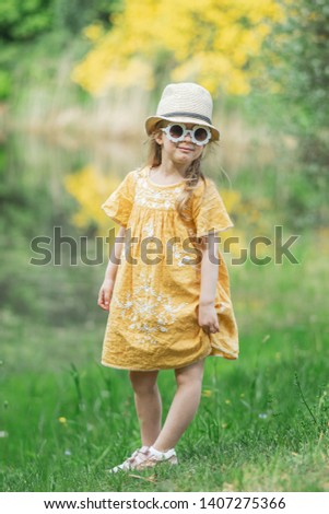 Cute little girl in white sunglasses playing with children's  wooden camera in the park with rhododendron flowers