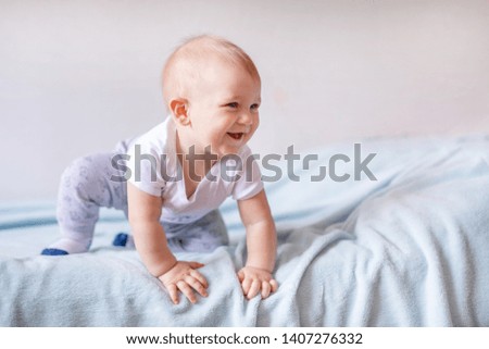 Adorable baby boy in white sunny bedroom. Newborn child relaxing on a blue bed. Nursery for young children. Newborn kid during tummy time with toys at a window.