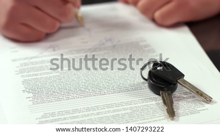Buyer hand signing rent agreement, transport keys on table closeup, insurance