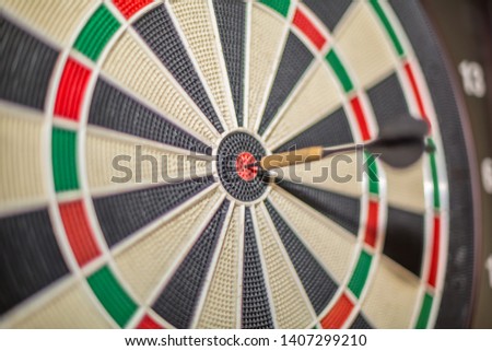 Accurate dart sight hitting center of target, dartboard and dart, blurred background...