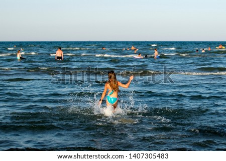 Girl on the beach in a swimsuit bathes in the sea. The girl turned her back to the camera.
