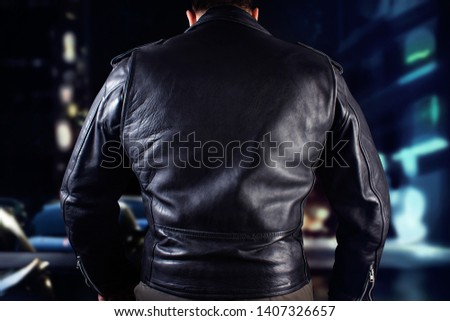 Closeup photo of a man in black leather biker jacket standing on black background. Royalty-Free Stock Photo #1407326657