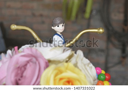 First Communion cake doll placed on a golden bicycle adorned with a bouquet of roses in its basket
