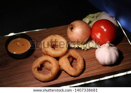 Onion rings with cheese sauce, onions, tomatoes on a wooden board