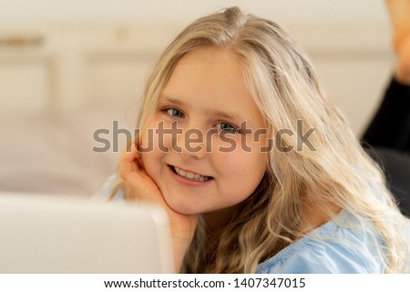 Beautiful cute happy blonde girl playing and surfing the internet on laptop. Child watching cartoon or video on laptop on the bed at home. Digital technology education and children internet usage.