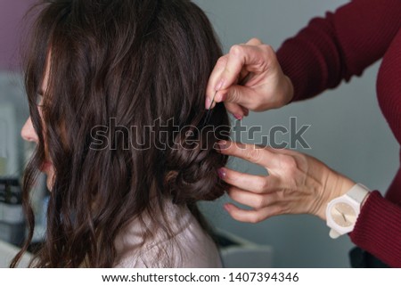 Preparation of bride. Hair creation process  brown-haired person girl, side-view long hair, hairstyle collected, styling in beauty salon. Master fixes lower beam of hair with invisible hairpins Royalty-Free Stock Photo #1407394346