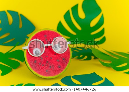 squishy toy watermelon in  glasses on yellow background among paper cut tropical leaves  