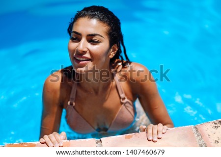 Happy young Arab woman relaxing in swimming pool. Smiling girl with healthy tanned skin and wet hair enjoying Summer Sun at pool edge.