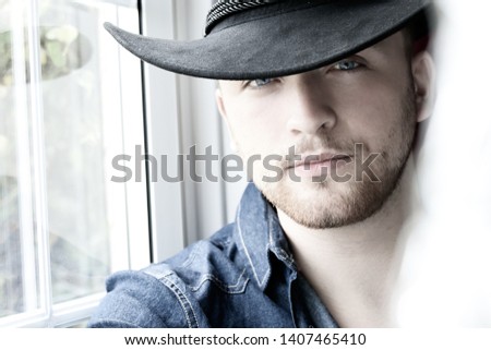 Portrait of handsome cowboy with blue eyes and hat looking at camera Royalty-Free Stock Photo #1407465410