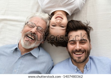Top view of happy three generations of men lying on bed looking at camera making photo together, portrait of smiling little son, father and grandfather posing for picture laughing relaxing at home Royalty-Free Stock Photo #1407480362