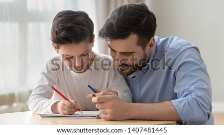Loving young dad sit at table with preschooler son spend time drawing in album together, smiling father enjoy leisure weekend painting picture learning with little boy child entertain at home