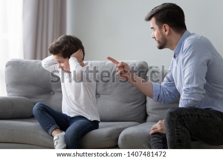 Angry young dad sit on couch lecture scold preschooler son closing ears with hands, offended stubborn boy child avoid ignore listening to serious mad father talking, having dispute or quarrel at home Royalty-Free Stock Photo #1407481472