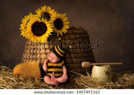 Sleepy cute baby in bee outfit resting against an antique beehive