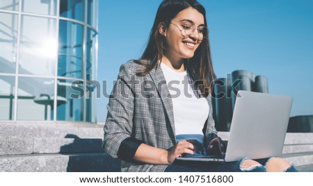 Happy young hipster girl in spectacles spending free time for cleaning mail messages via modern laptop device feeling good from found email with discounts for online shopping in web store