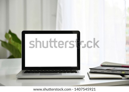 Laptop empty screen on white table with notebook paper.