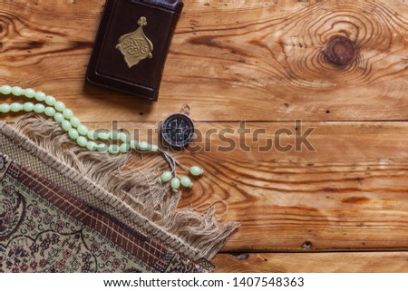 Traditional muslim prayer set bundle. Praying carpet, rosary beads, little version of the Holy Quran and qibla compass on wooden background. Copy Space Royalty-Free Stock Photo #1407548363