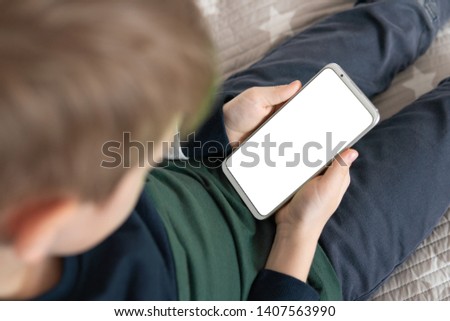 Smartphone with a white screen in hand child . Smartphone with a mock up in the hands of a child. close up top view Phone a for mock up is holding kid.