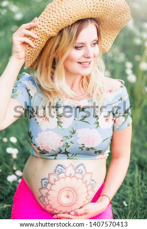 pregnant woman with mehendi pattern on her belly is sitting on the field with dandelions