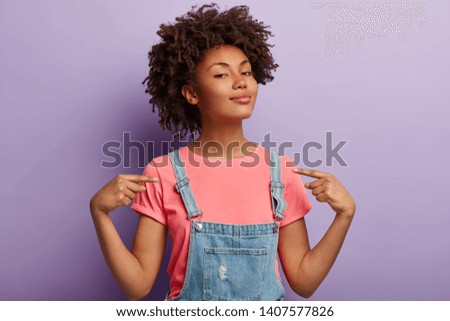 People, pride, arrogance concept. Self assured proud woman has Afro hairstyle satisfied with own high achievements, feels confident, keeps head raised, being like hero, isolated on purple wall Royalty-Free Stock Photo #1407577826