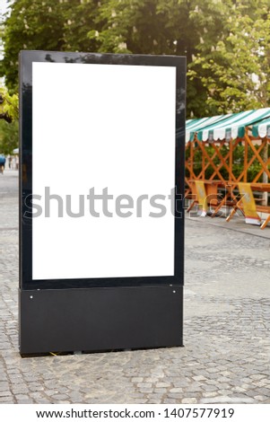 Vertical street billboard with white copy space, black thick edges on city background. Black lightbox on pavement. Modern panel. Signboard for your advertisement, text or design. Outdoor signing.