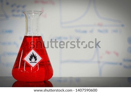 Erlenmeyer flask with Red liquid and chemical hazard warning symbols labels (flammable sign) on whiteboard with chemical learning background.