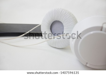 White headphones and black phone on a light background isolated