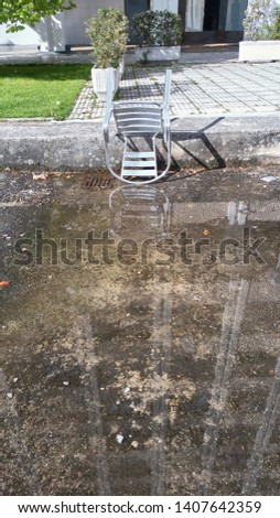 Aluminum chair upside down resting on a concrete block in front of a puddle on an urban street