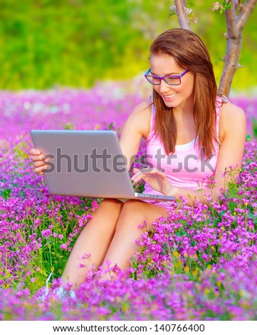 Cute woman sitting down in beautiful floral garden with laptop, wearing glasses, working outdoors, studying on university backyard, business and success concept