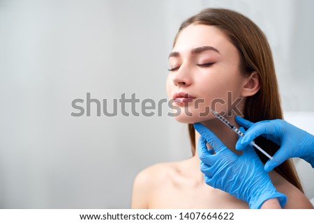 Smile lifting and lip augmentation. Beautician doctor hands doing beauty procedure to female face with syringe. Young woman's mouth countouring with filler injection. Marionette lines treatment. Royalty-Free Stock Photo #1407664622