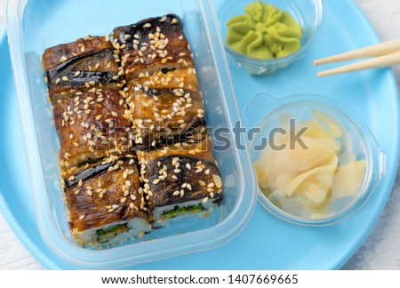 portion of rolls with eel with wasabi and ginger on a plastic blue plate on a white table
